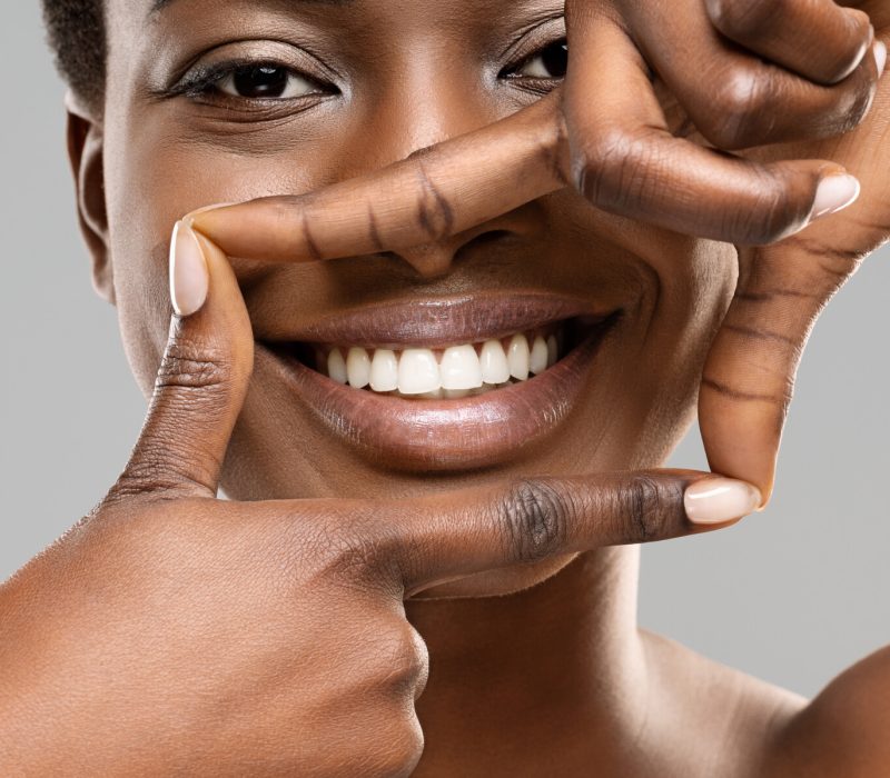 Frame your smile. Beautiful african woman framing her perfect white teeth with fingers, closeup