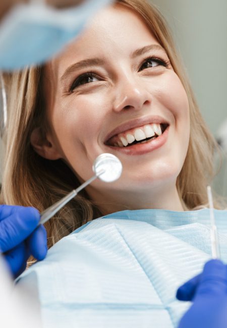 Image of pretty young woman sitting in dental chair at medical center while professional doctor fixing her teeth